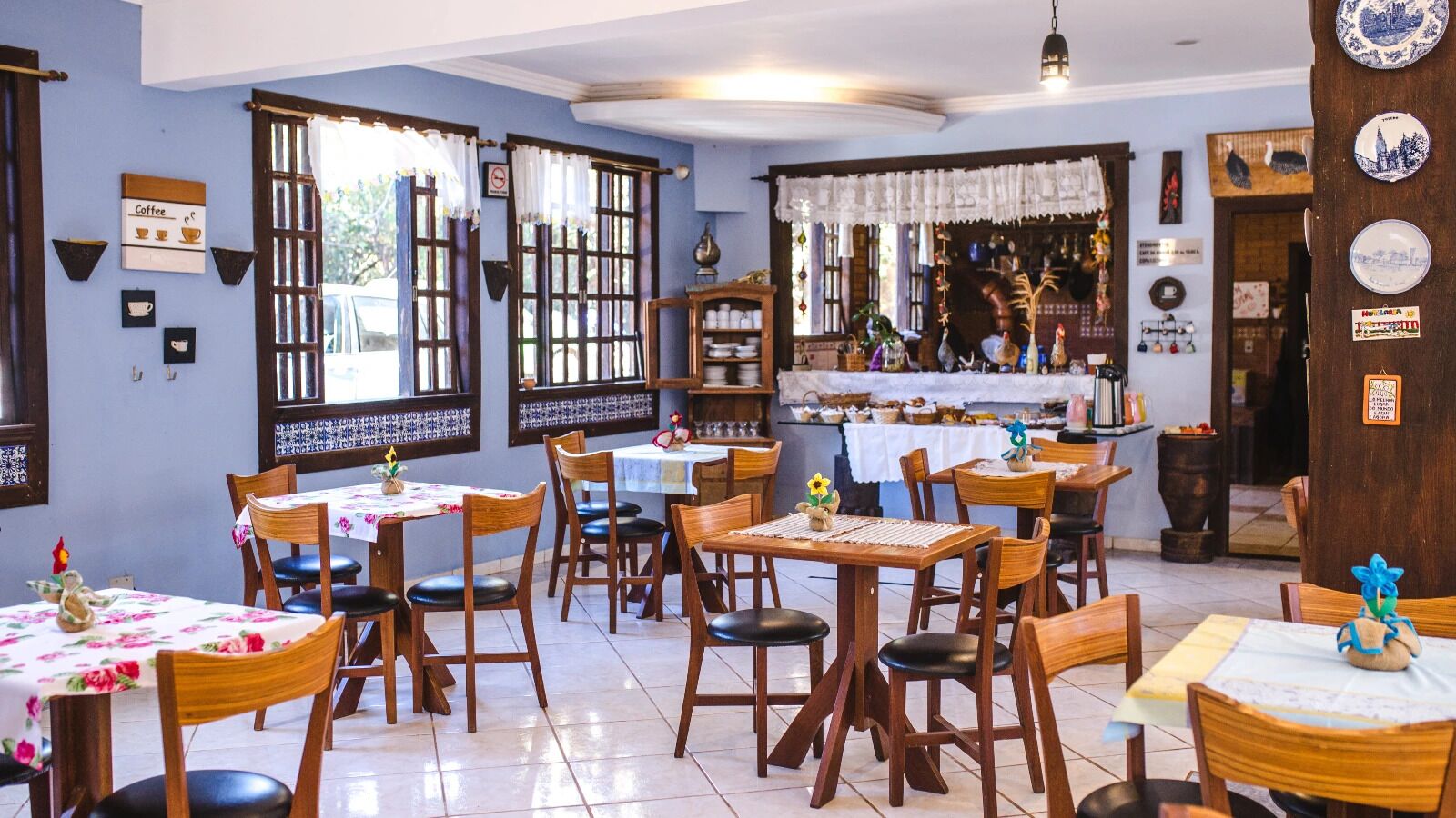 Um restaurante com mesas e cadeiras de madeira, área de bar e pratos decorativos na parede.