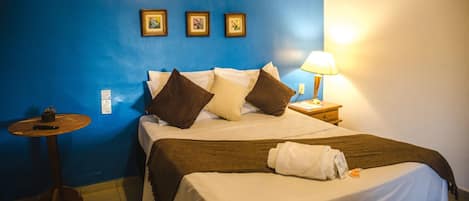 Habitación de hotel con una cama, una mesita de noche, una lámpara y tres cuadros en la pared.
