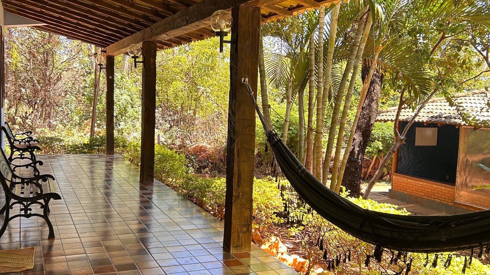 A covered outdoor area with a hammock, a bench, and a tiled floor.