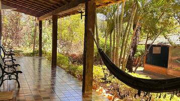 A covered outdoor area with a hammock, a bench, and a tiled floor.