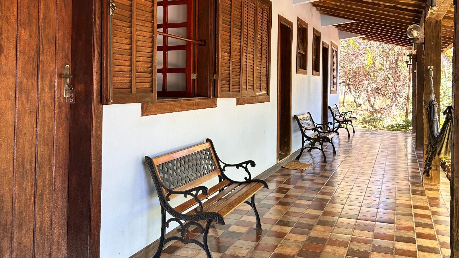 A covered corridor with wooden benches, a tiled floor, and wooden-framed windows.
