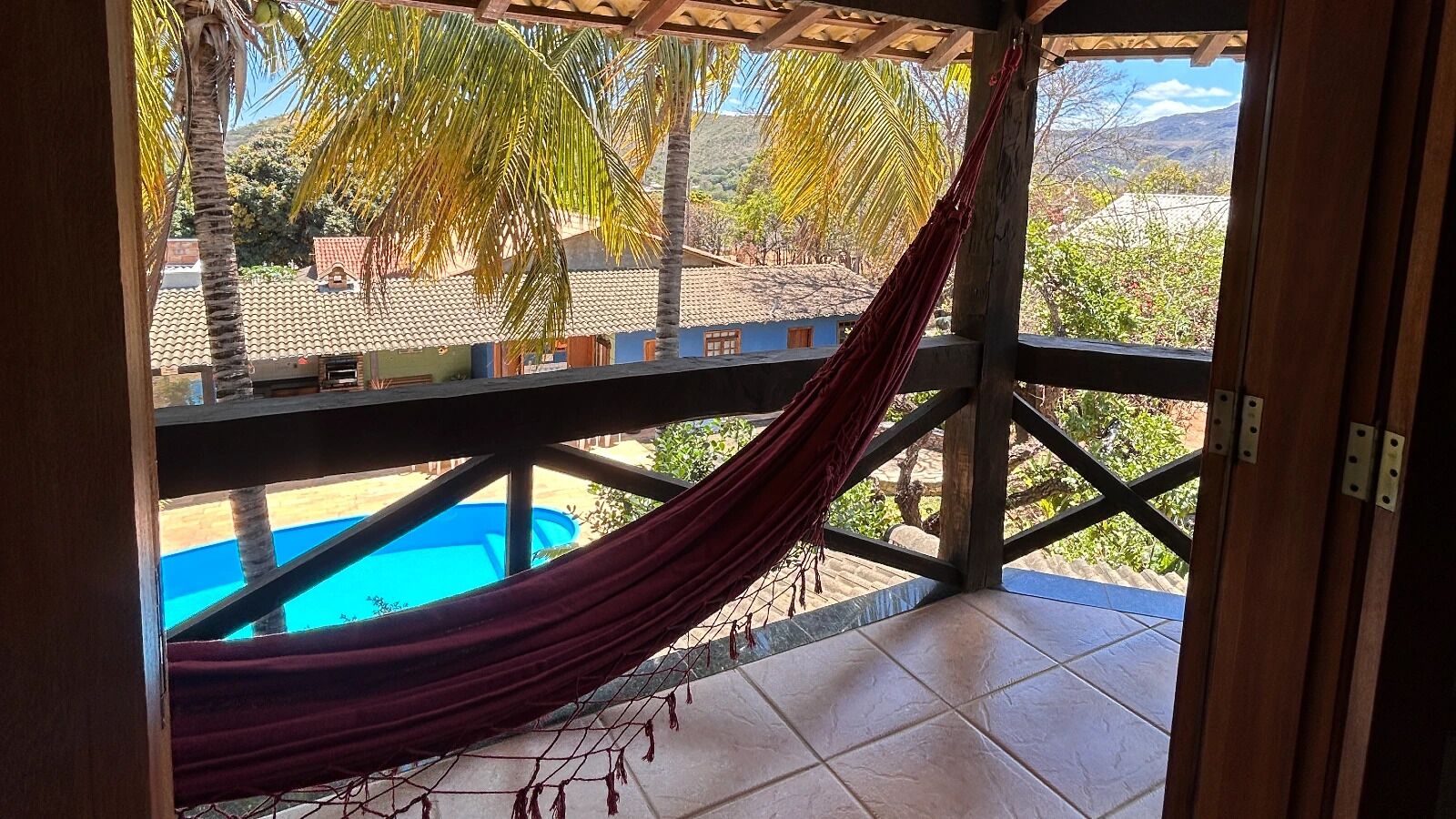 A hammock on a balcony with a view of a swimming pool and palm trees.