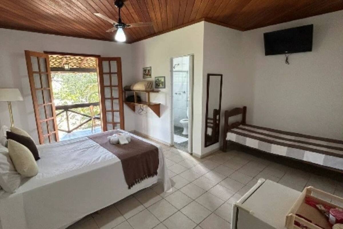 Quarto com cama, escrivaninha, cadeira, televisão e varanda.
