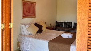 A hotel room with a bed, pillows, a bedside table, a nightstand, a blanket, and a painting on the wall. - Pousada Recanto (Santana do Riacho)