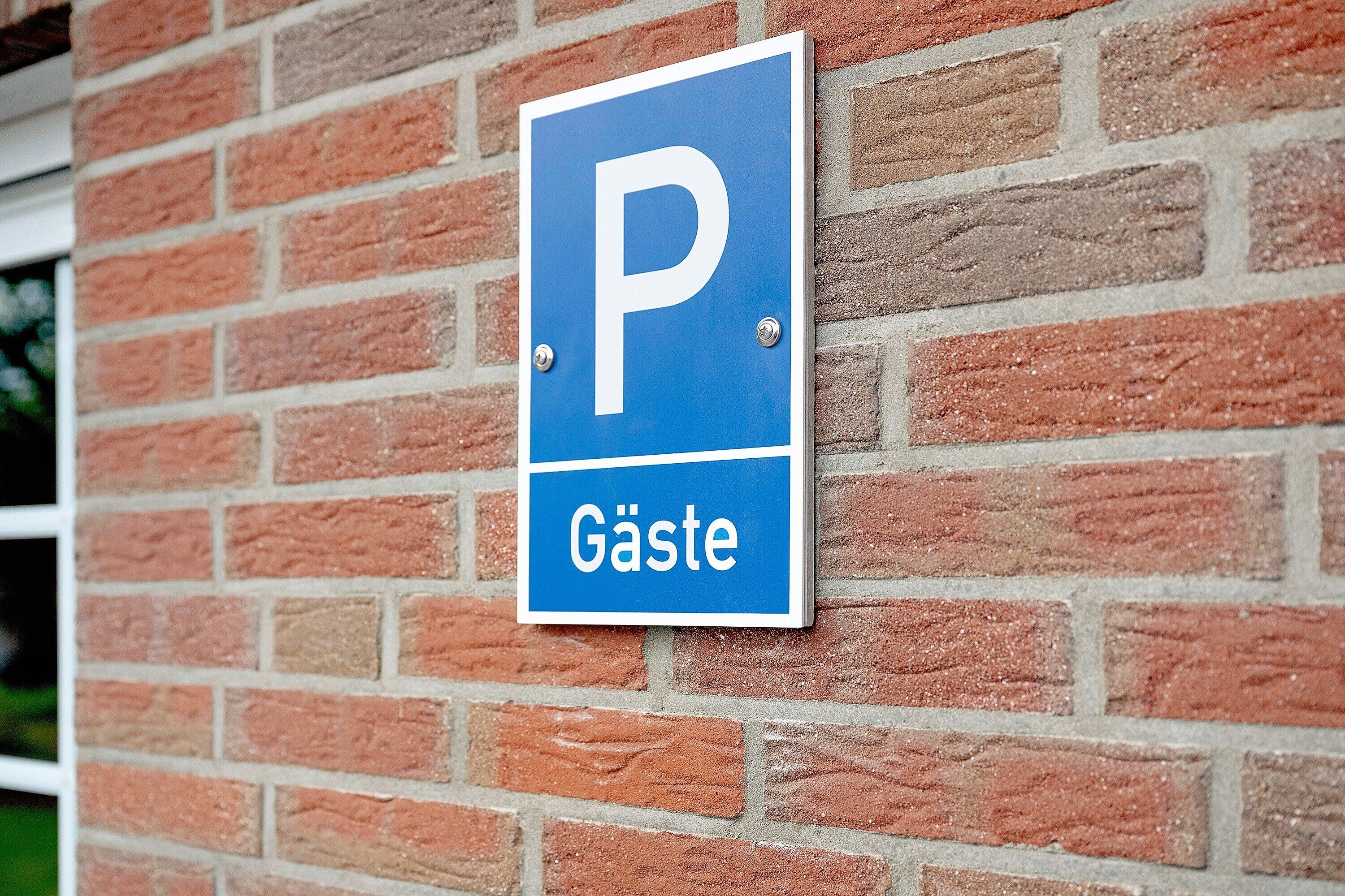A blue parking sign with a white 'P' and the word 'Gäste' on a brick wall.