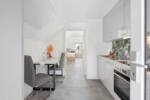 Eine moderne Küche mit weißen Schränken, einem Essbereich mit Tisch und Stühlen sowie einem sichtbaren Backofen.