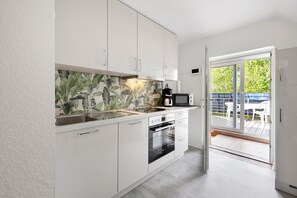 Una cocina moderna con armarios blancos, horno empotrado y un amplio ventanal con acceso a un patio exterior.