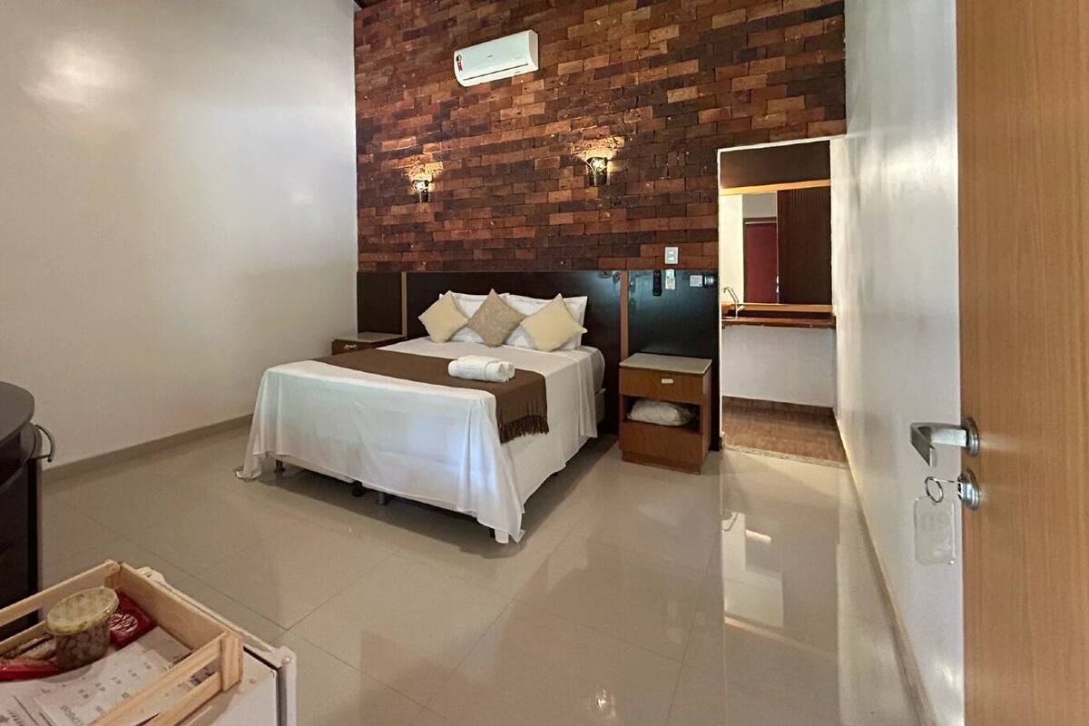A hotel room with a bed, nightstands, a desk, and a brick wall.
