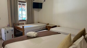 A room with two single beds, a small refrigerator, a TV mounted on the wall, and a window with curtains.