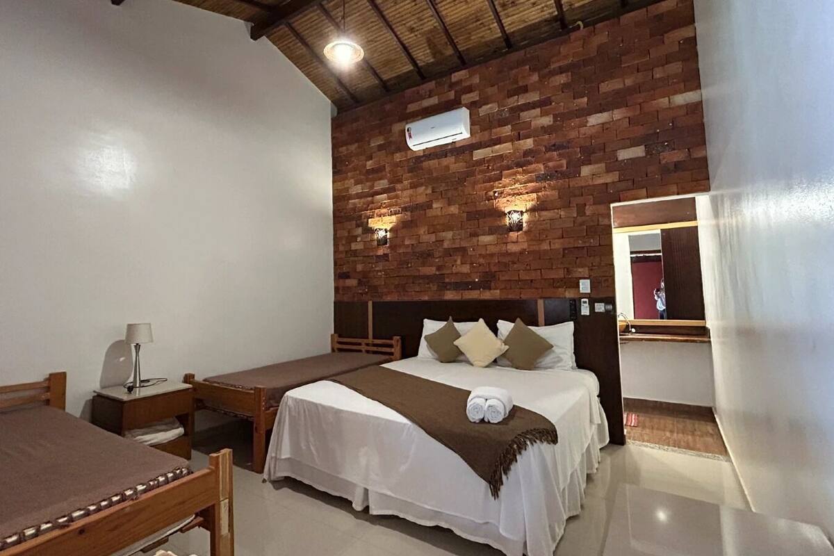 A room with two beds, a wooden table, a lamp, and a brick wall.