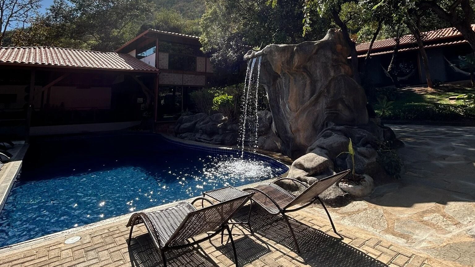 A swimming pool with a waterfall feature, lounge chairs, and a building with a tiled roof.