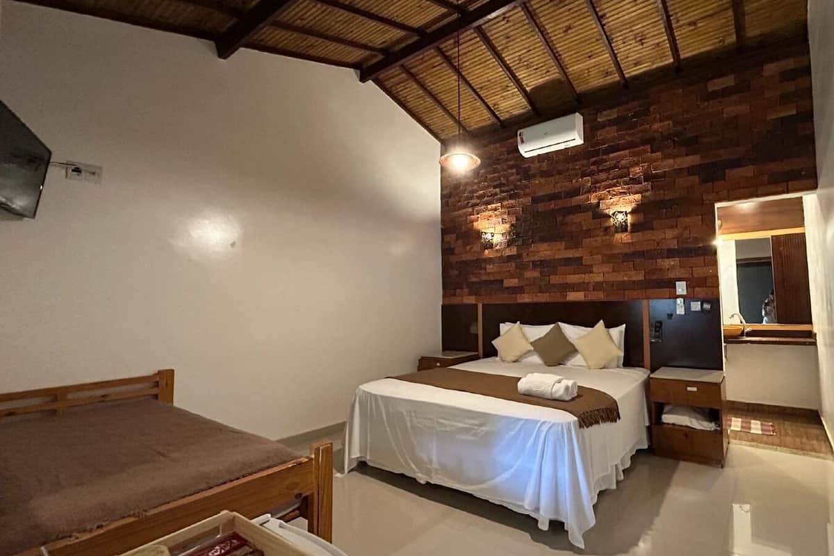 A bedroom with a bed, a bedside table, a nightstand, a mirror, and a brick wall.