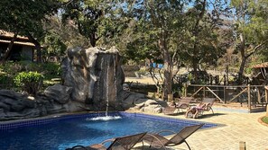 A swimming pool with a waterfall feature, lounge chairs, and a covered seating area.