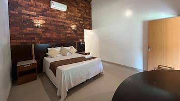 Hotellihuone, jossa on tiiliseinä, valkoisilla lakanoiden peitetty sänky, yöpöytä, sängyn vieressä oleva pöytä, pyöreä pöytä ja ovi.