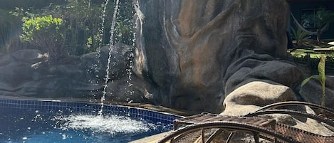 Una piscina con una cascada, rodeada de rocas y un borde de azulejos.