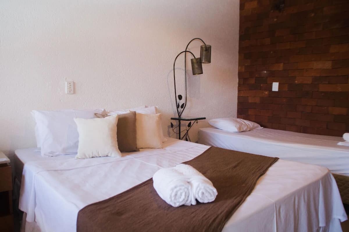 A hotel room with two beds, white bedding, a brown throw blanket, and a wall-mounted lamp.