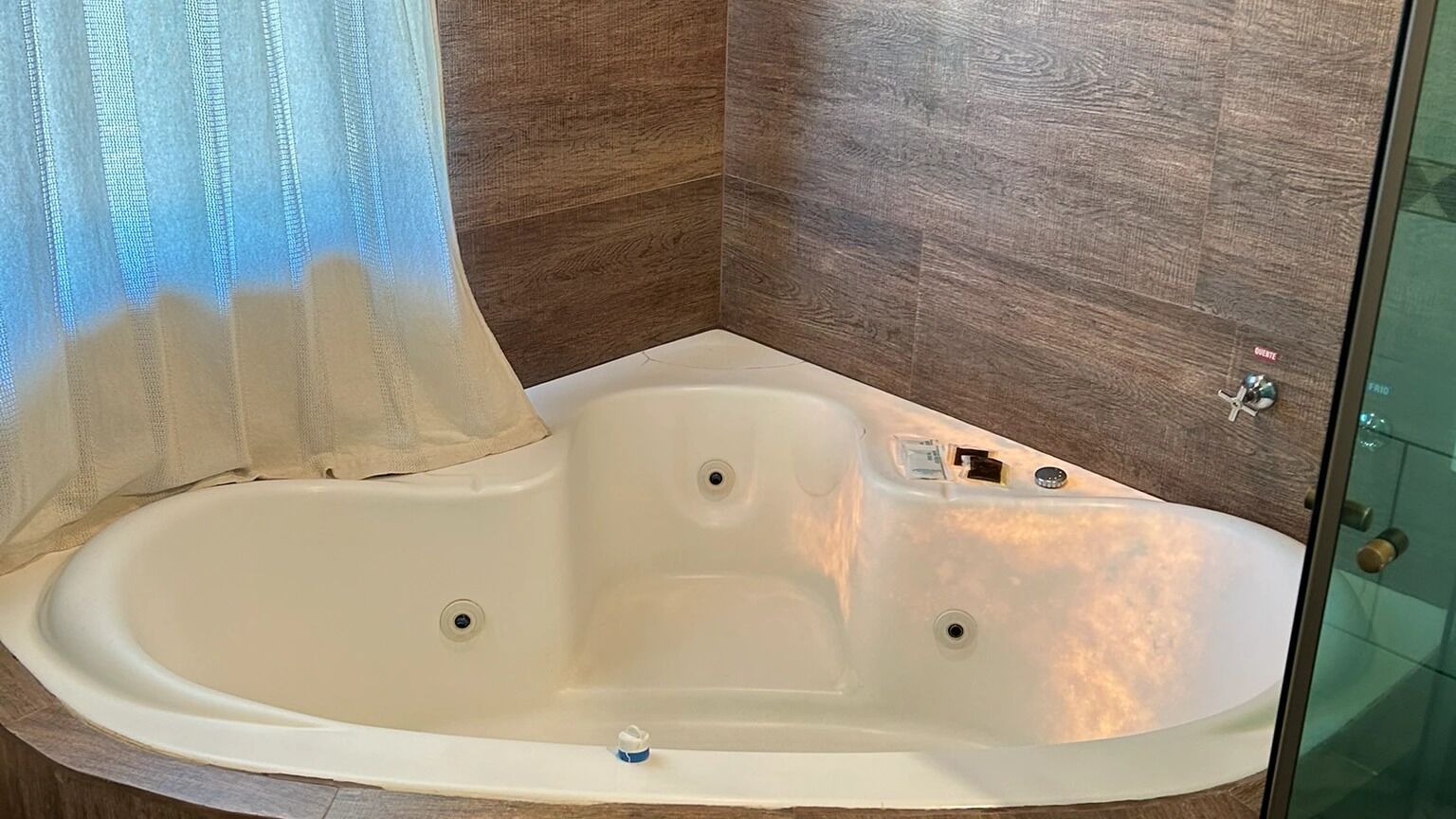 Una bañera en una esquina, paredes de madera y cabina de ducha de vidrio.