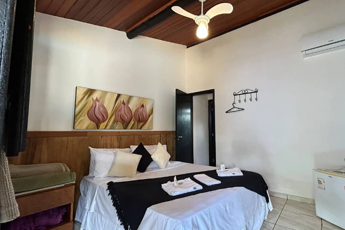 A hotel room with a bed, a small desk, a TV, a heater, and a painting on the wall.