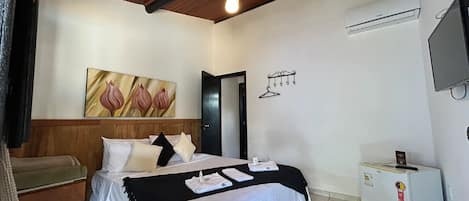 A hotel room with a bed, a small desk, a TV, a heater, and a painting on the wall.