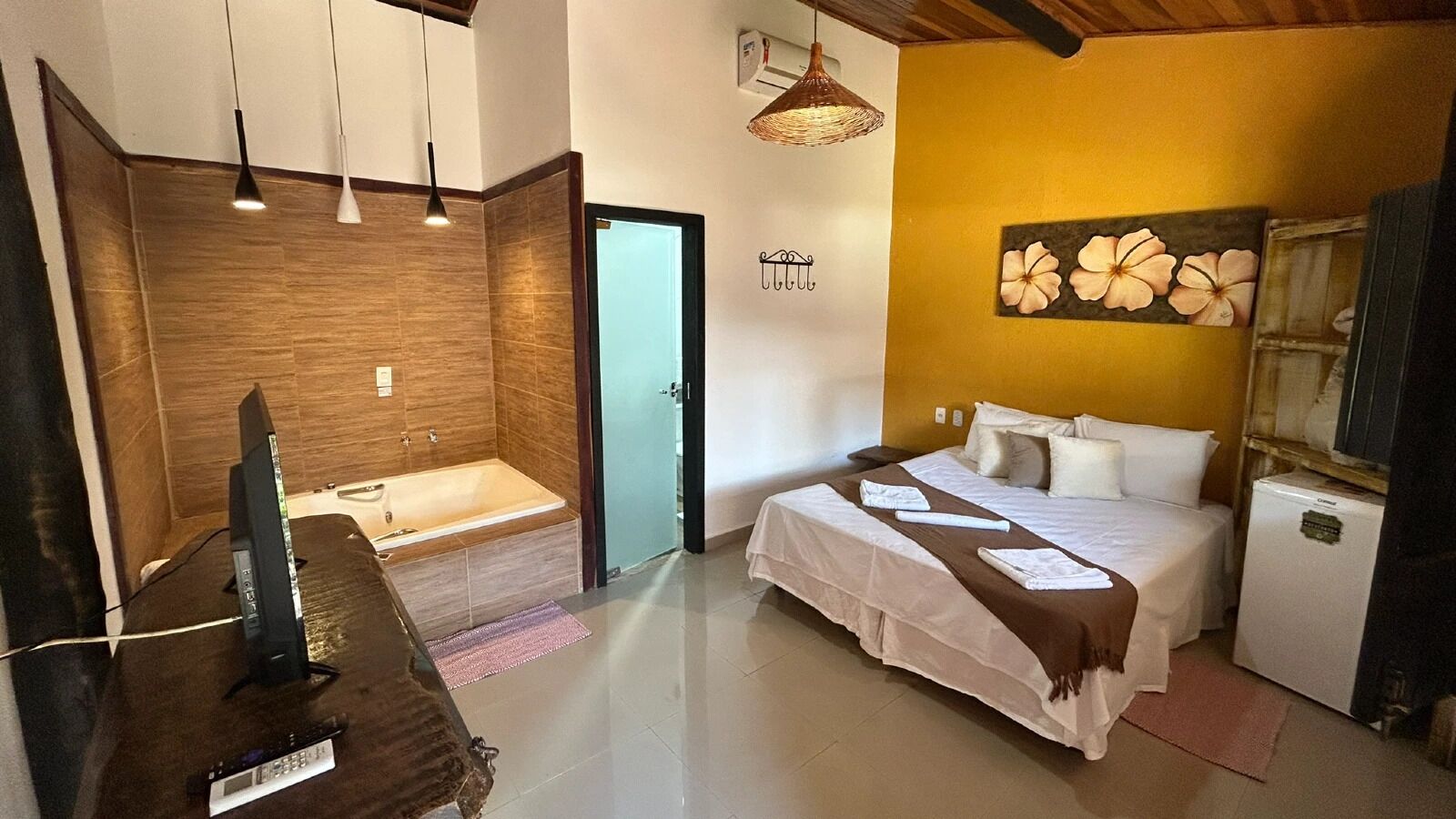 A hotel room with a bed, a small desk with a computer, a bathtub, and a wall-mounted artwork.