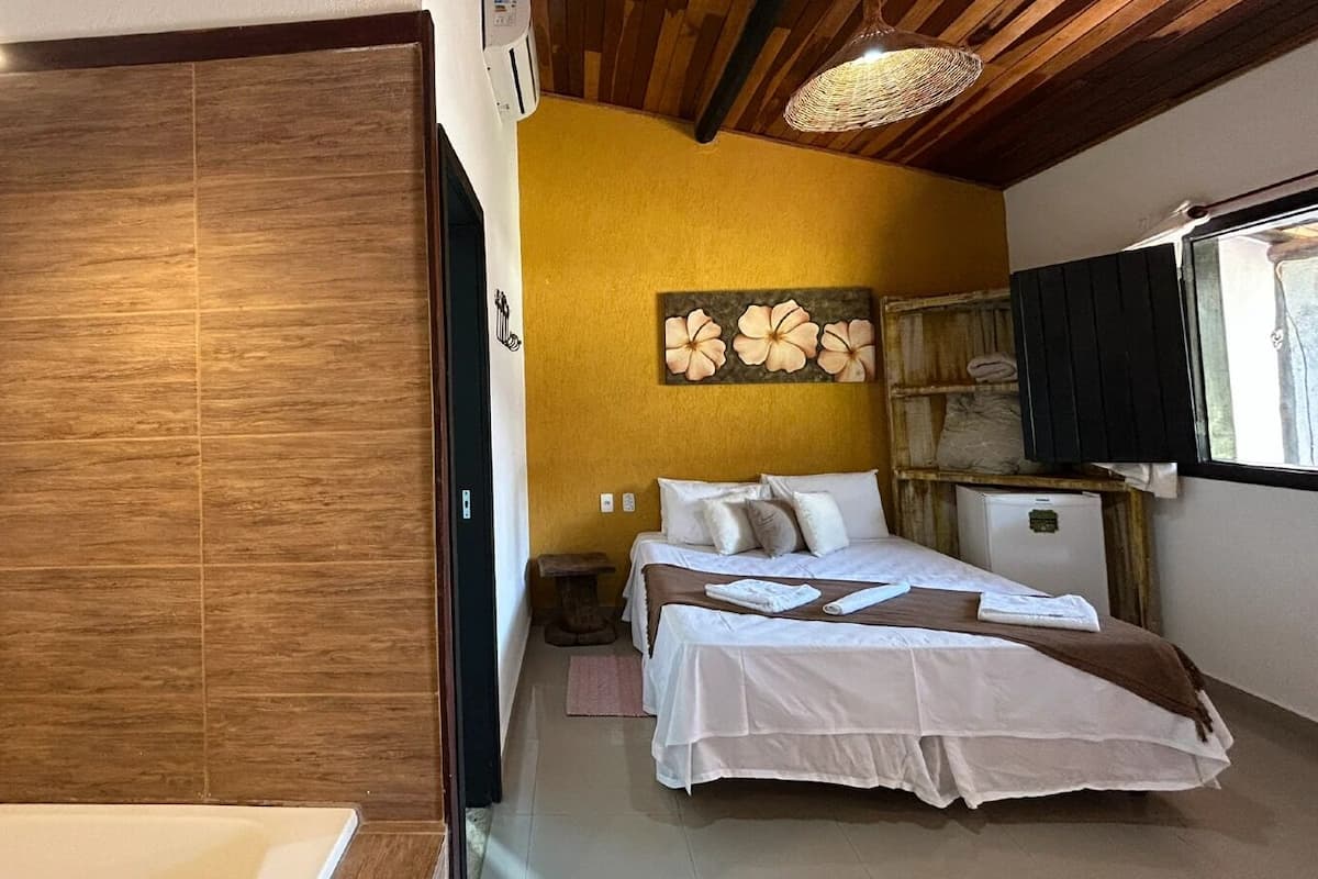 A bedroom with a bed, a bedside table, a nightstand, a wall-mounted artwork, and a window with blinds.
