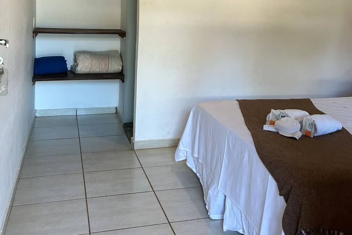 A hotel room with a bed, a bench with pillows, and a door with a key in the lock.