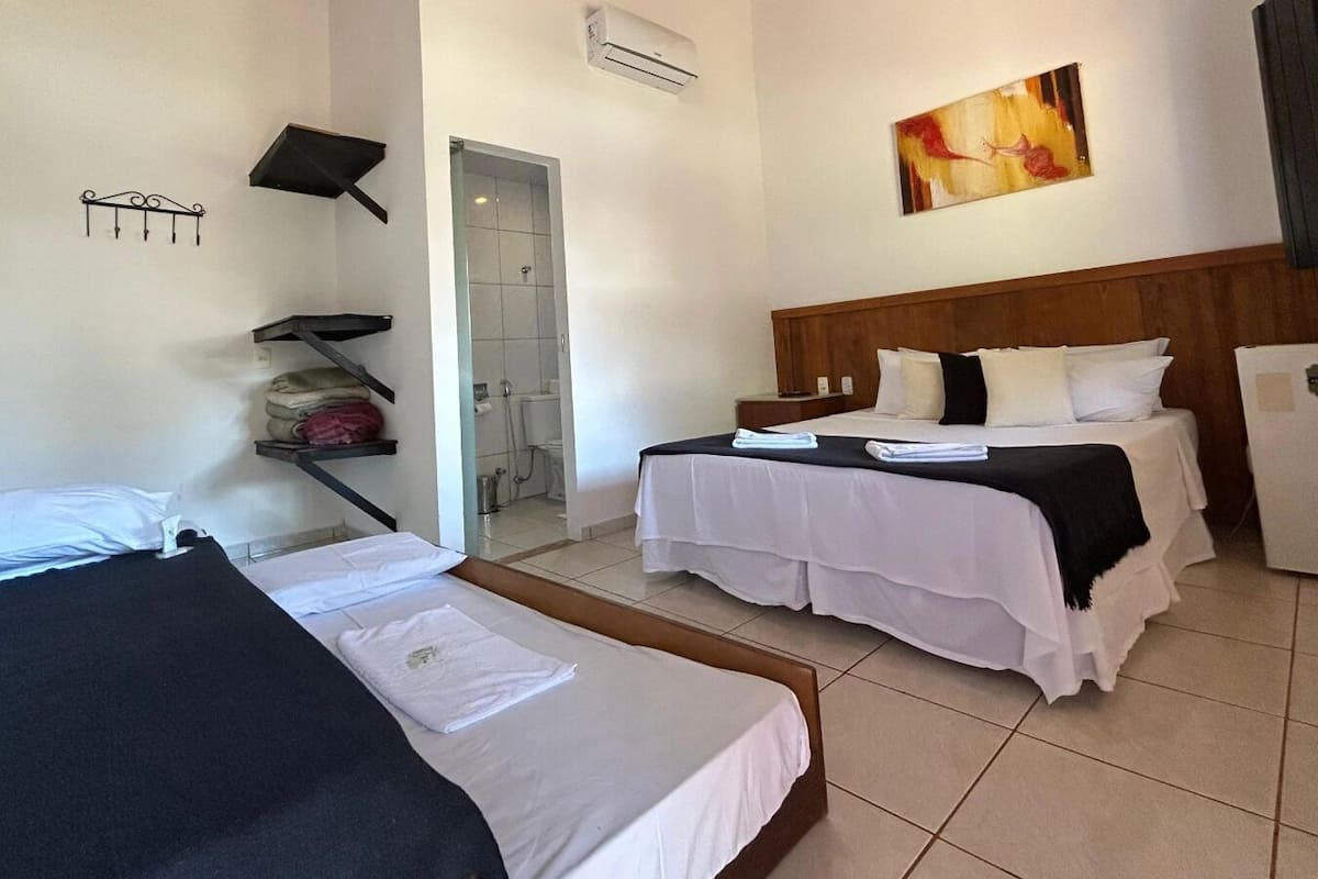 A hotel room with two beds, a shower area, a refrigerator, and a painting on the wall.