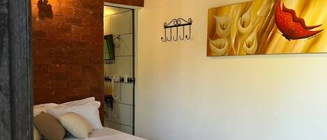 A hotel room with a bed, a painting, a telephone, and a brick wall.