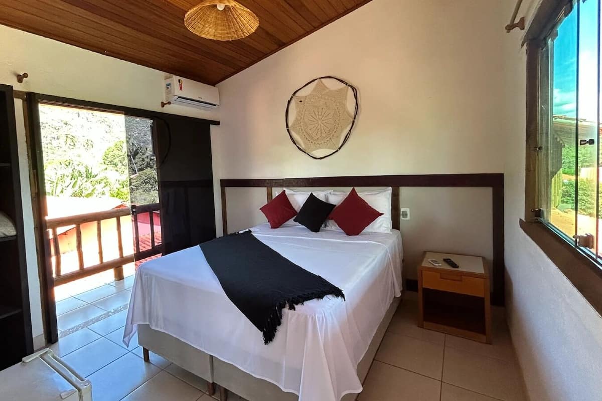 A bedroom with a bed, pillows, a bedside table, a wall hanging, and a window.