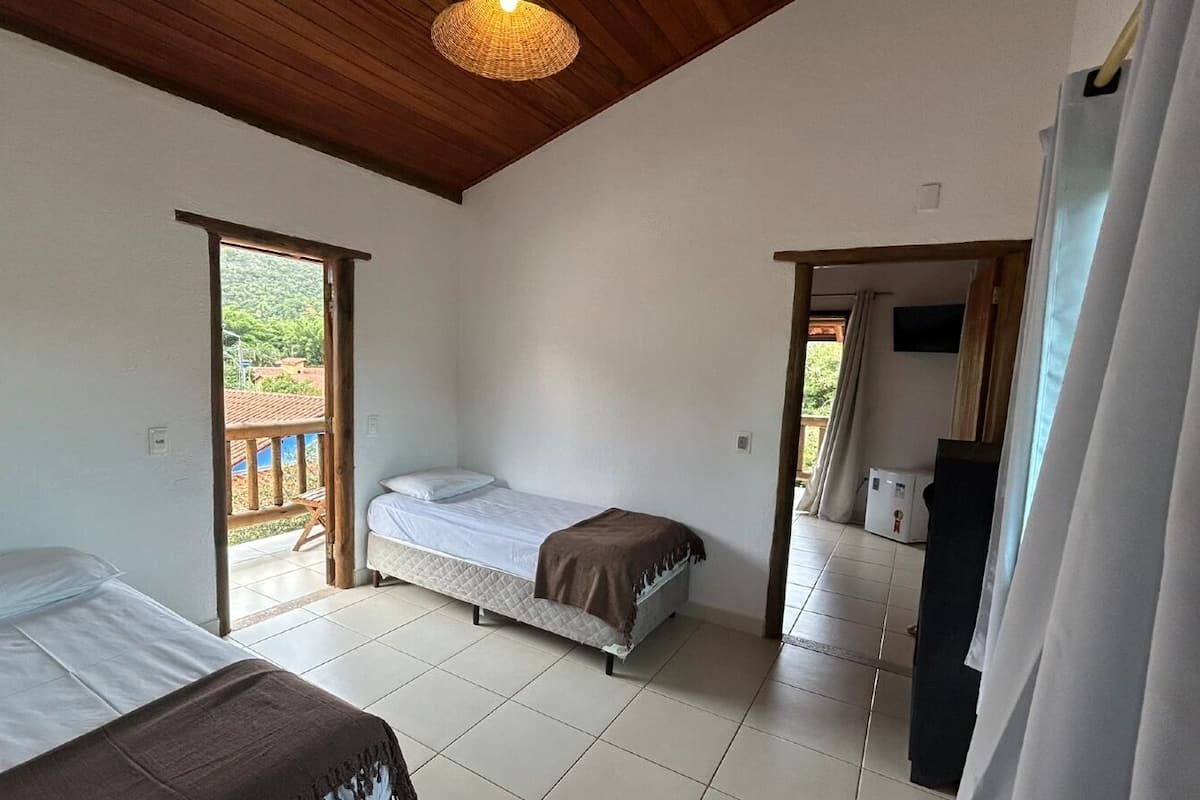 A bedroom with two beds, a wooden ceiling, and a view through an open door.