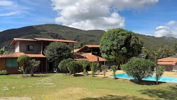 A residential property with a swimming pool, multiple buildings, and a mountainous backdrop.