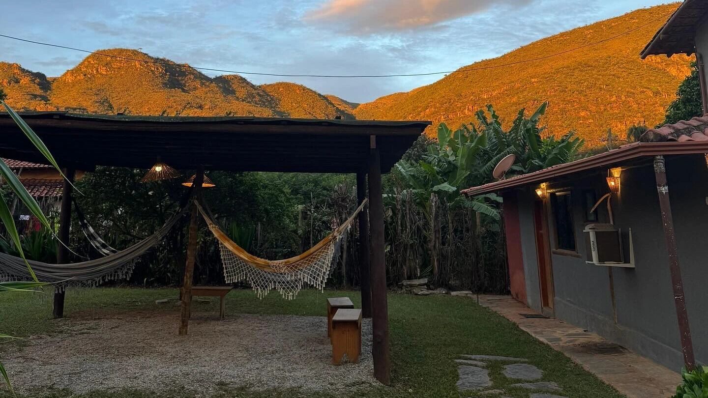 Una hamaca bajo una zona cubierta, un banco pequeño y un edificio con antena parabólica.