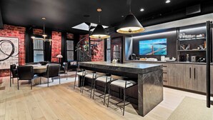A modern kitchen with a large island, bar area, and a TV displaying a scenic view. - RoofTopPatio–HotTub–FirePit-WetBar-Downtown (Cleveland)