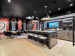 A modern kitchen with a large island, bar area, and a TV displaying a scenic view. - RoofTopPatio–HotTub–FirePit-WetBar-Downtown (Cleveland)