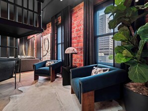 A modern living room with a brick wall, a large window, a sofa, a chair, a lamp, and a potted plant. - RoofTopPatio–HotTub–FirePit-WetBar-Downtown (Cleveland)