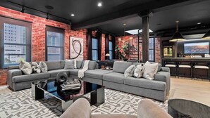 A modern living room with a sectional sofa, a coffee table, and a bar area with stools. - RoofTopPatio–HotTub–FirePit-WetBar-Downtown (Cleveland)