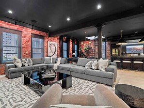 A modern living room with a sectional sofa, a coffee table, and a bar area with stools. - RoofTopPatio–HotTub–FirePit-WetBar-Downtown (Cleveland)