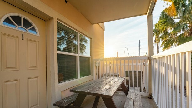 A covered patio with a wooden table and benches, a white fence, and a house entrance. - Star Beachside - Marlin Cottages 1 - Beautiful Condo, Family Friendly, Swimming & Kiddie Pool, Spa, Short Walk to the Beach (South Padre Island)