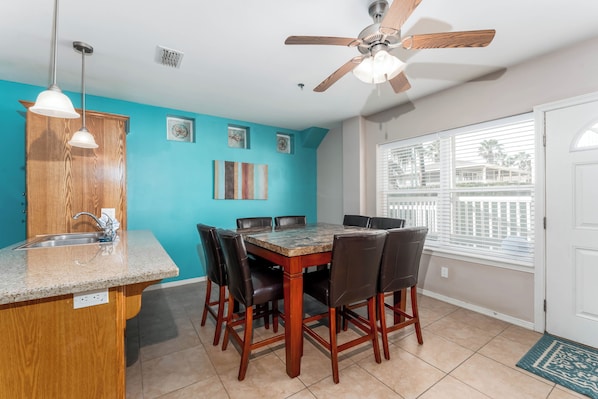 A kitchen with a dining table, chairs, a ceiling fan, and a window with blinds. - Star Beachside - Marlin Cottages 1 - Beautiful Condo, Family Friendly, Swimming & Kiddie Pool, Spa, Short Walk to the Beach (South Padre Island)