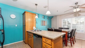 A kitchen with a teal wall, wooden cabinets, a dishwasher, a granite countertop, and a dining area with chairs. - Star Beachside - Marlin Cottages 1 - Beautiful Condo, Family Friendly, Swimming & Kiddie Pool, Spa, Short Walk to the Beach (South Padre Island)
