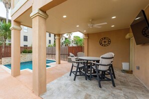 An outdoor patio with a pool, a table with chairs, a ceiling fan, and a clock on the wall.