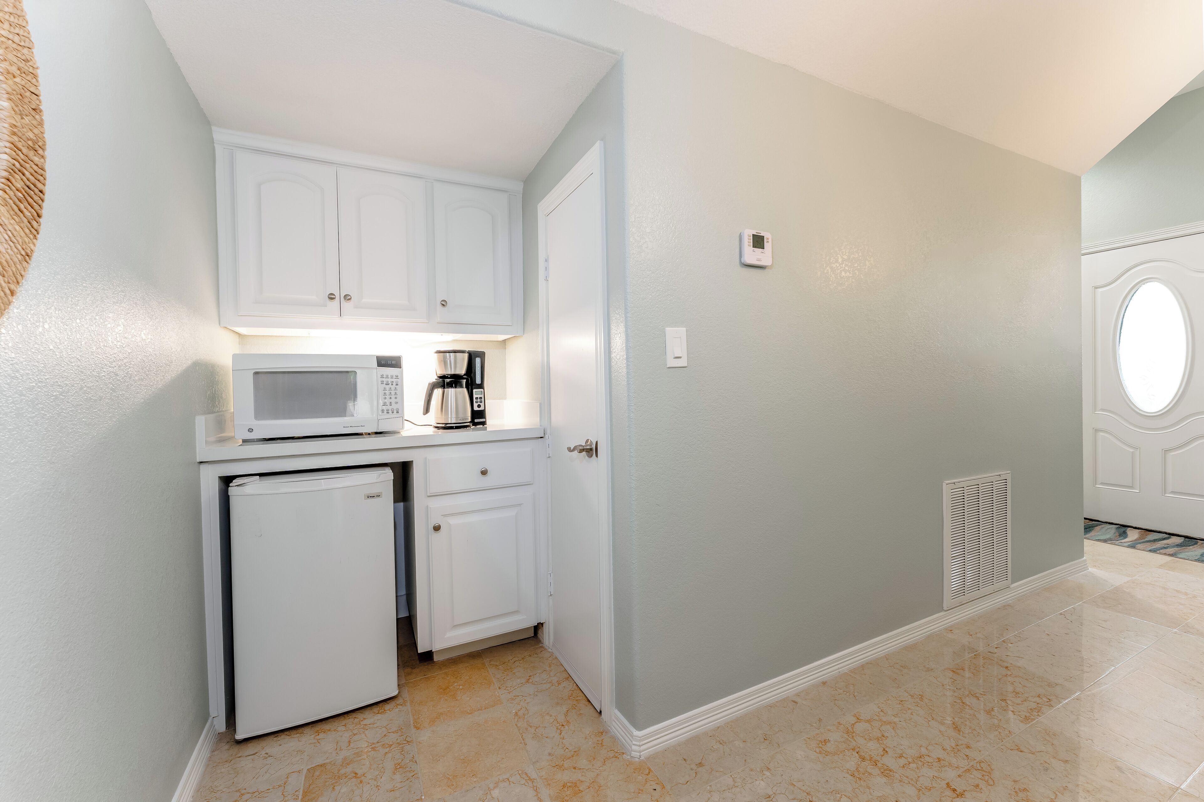 A compact kitchen with white cabinets, a microwave, a coffee maker, and a small refrigerator.