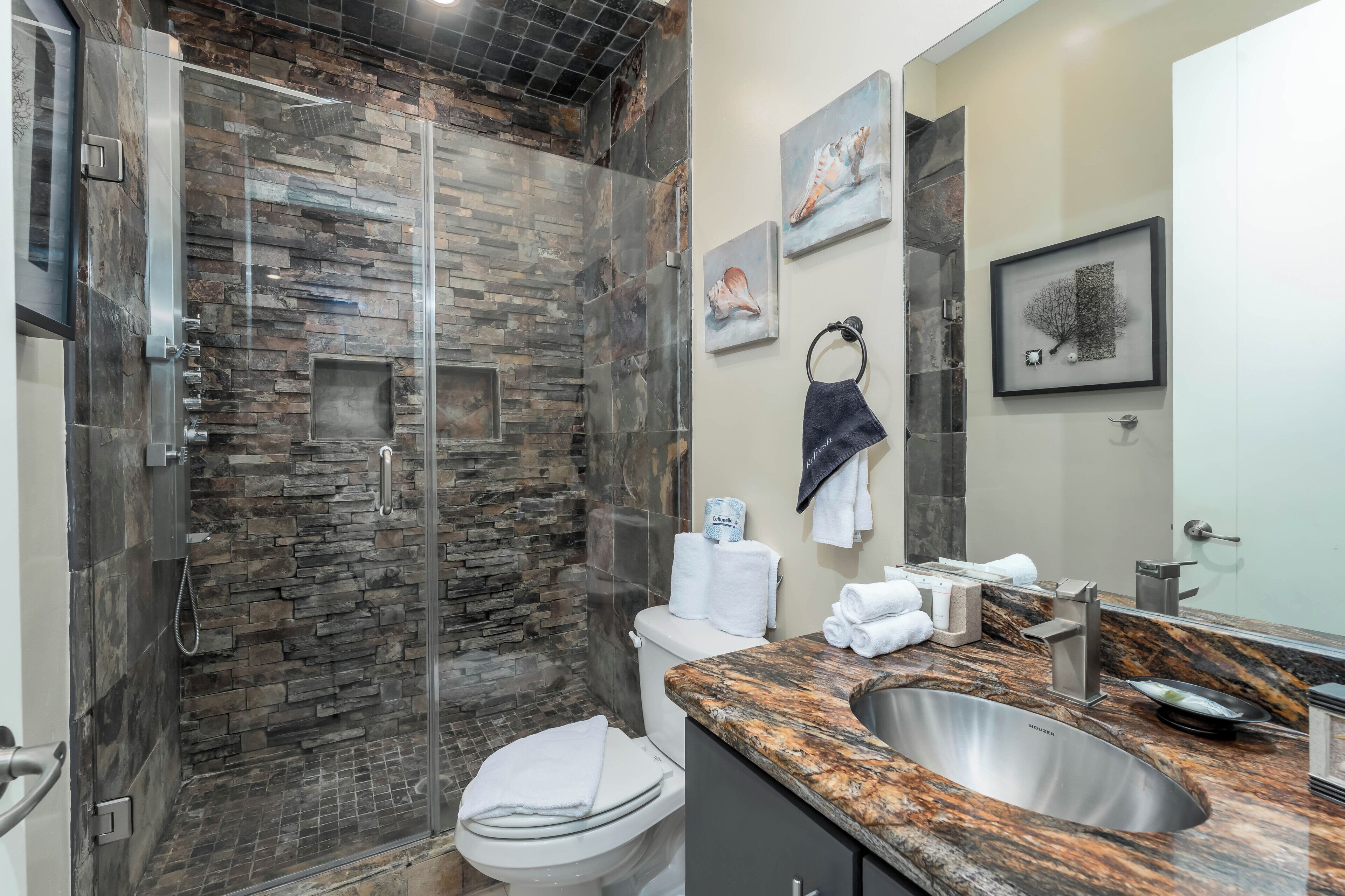 A modern bathroom with a glass-enclosed shower, a marble sink, and a toilet.