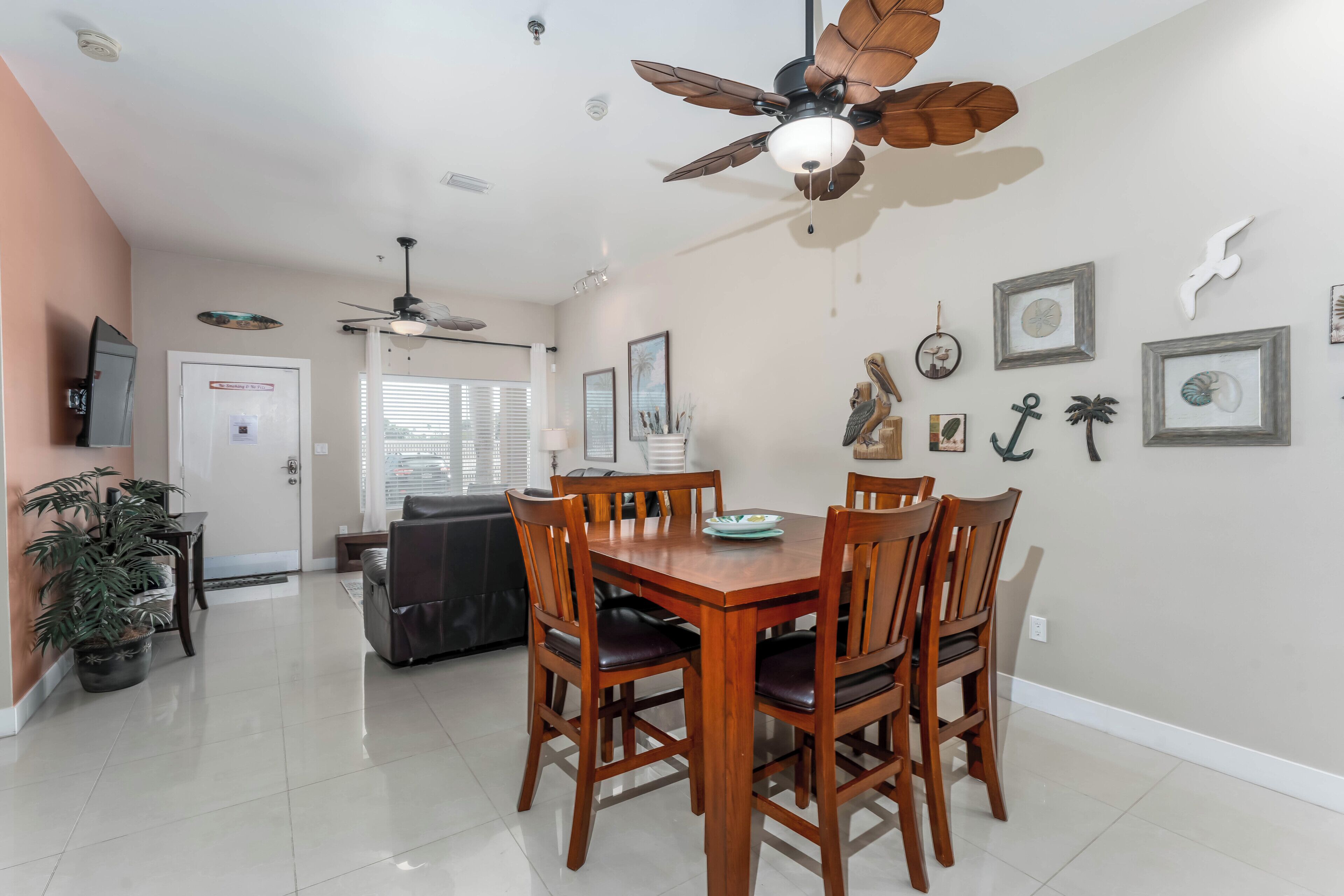 A dining area with a wooden table and chairs, a ceiling fan, and wall-mounted artwork.
