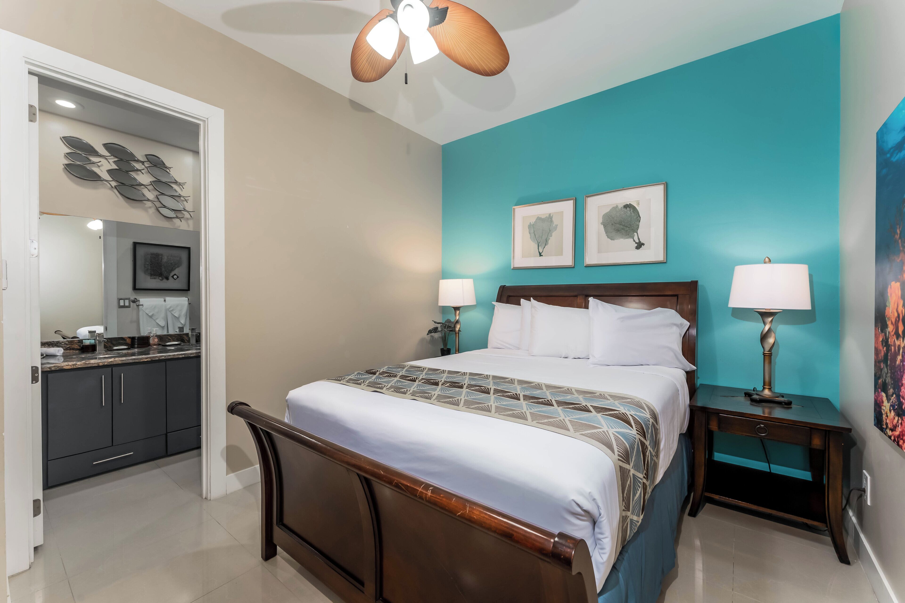 A bedroom with a bed, nightstands, a ceiling fan, and artwork on the walls.