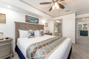 Ein Schlafzimmer mit einem großen Bett, einem Deckenventilator und Blick ins Badezimmer.