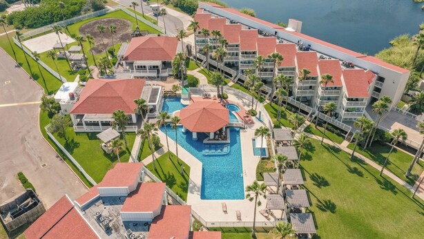 Vista aerea di un resort con una piscina centrale, diversi edifici con tetti rossi e palme.