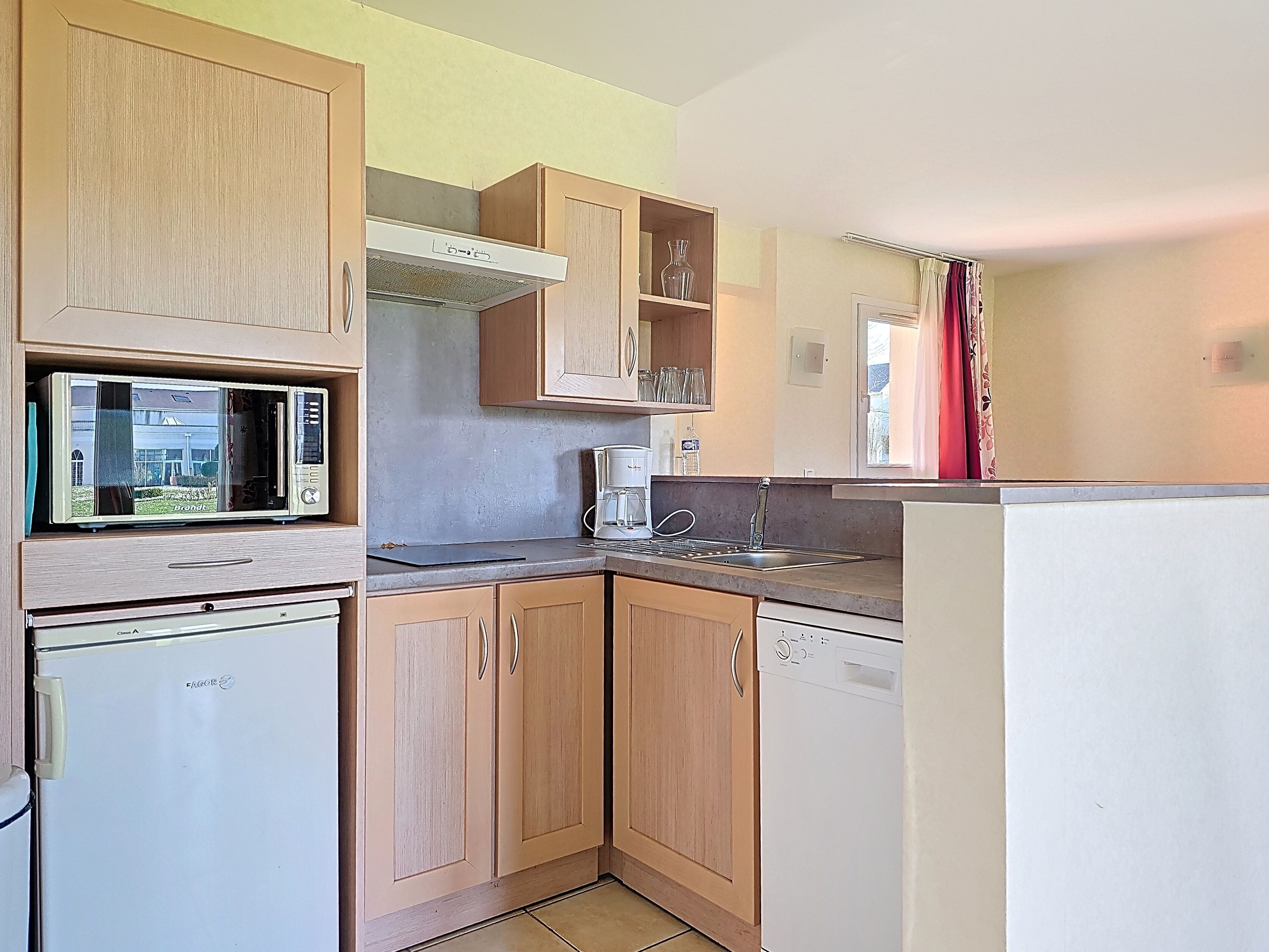 A compact kitchen with wooden cabinets, a microwave, a coffee maker, and a dishwasher.