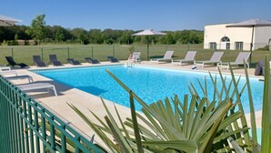 A swimming pool with lounge chairs and umbrellas, surrounded by a green fence and palm trees. - Terres de France - Domaine Val d'Amboise (Amboise)