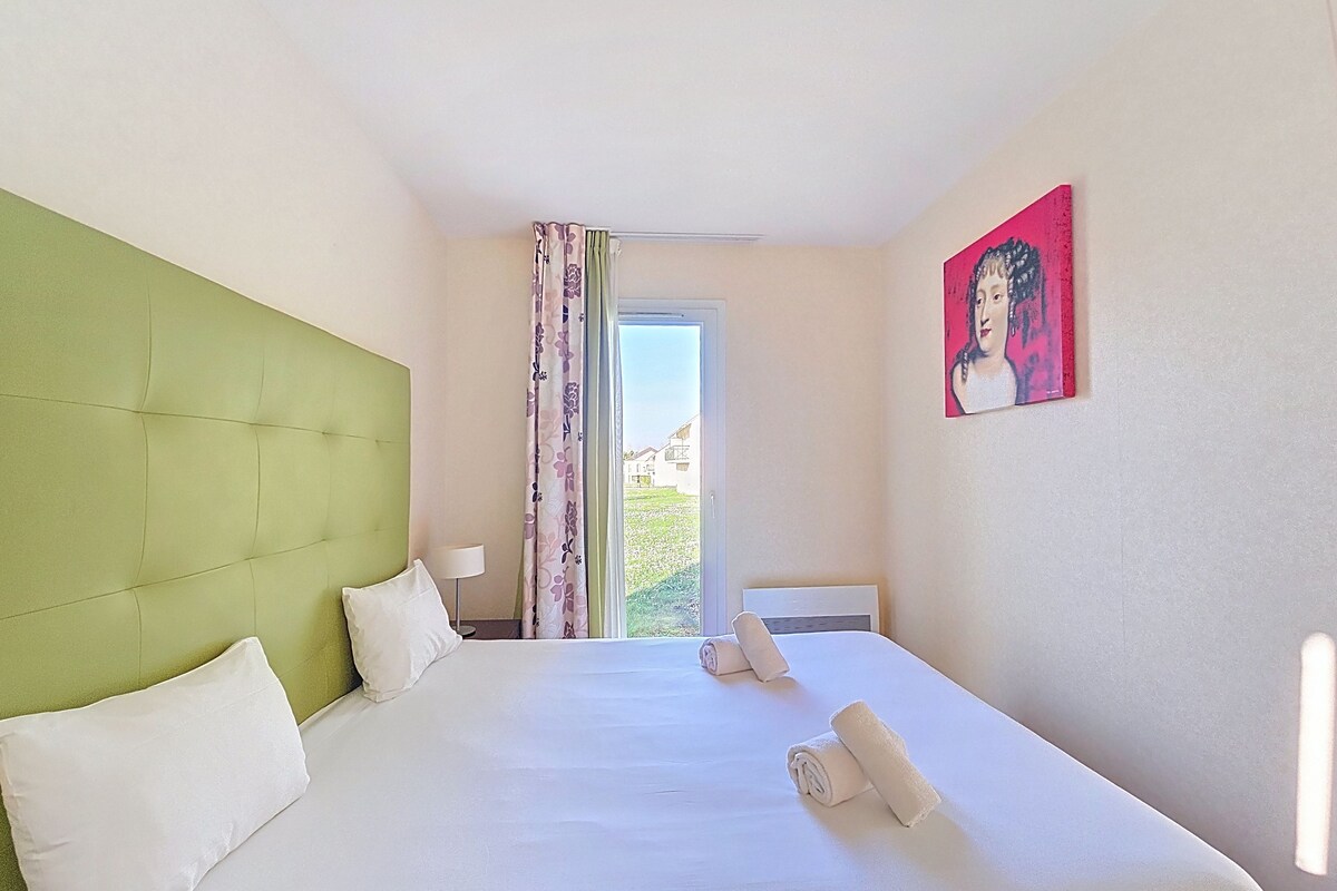 A hotel room with a green headboard, a bed with white linens, a painting on the wall, and a window with curtains.